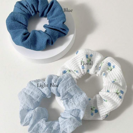 Light blue scrunchie and white floral scrunchie flat lay on white background