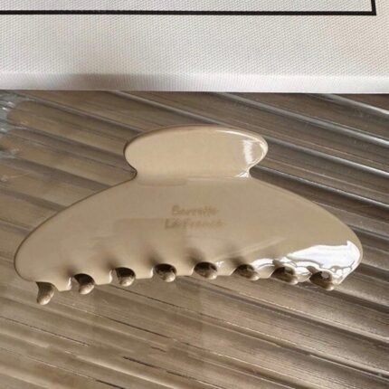 Glossy beige claw clip hair accessory on textured surface